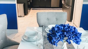 Une cuisine moderne avec des meubles de couleur sombre, un réfrigérateur en acier inoxydable et un coin repas agrémenté d’assiettes blanches et de fleurs bleues.