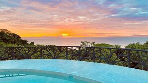 A sunset view from a balcony with a pool.