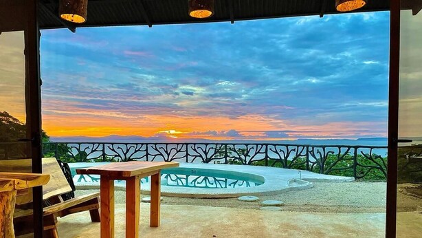 A view from a balcony with a sunset, a wooden table, and a decorative fence.
