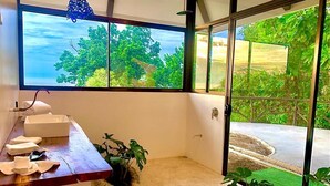 A modern bathroom with a large window, a wooden counter, and a potted plant.