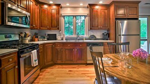 A kitchen with wooden cabinets, stainless steel appliances, a window, and a dining table with chairs. - 3 Mi to Beaches: Tranquil Cape Cod Escape w/ Deck (Bourne)