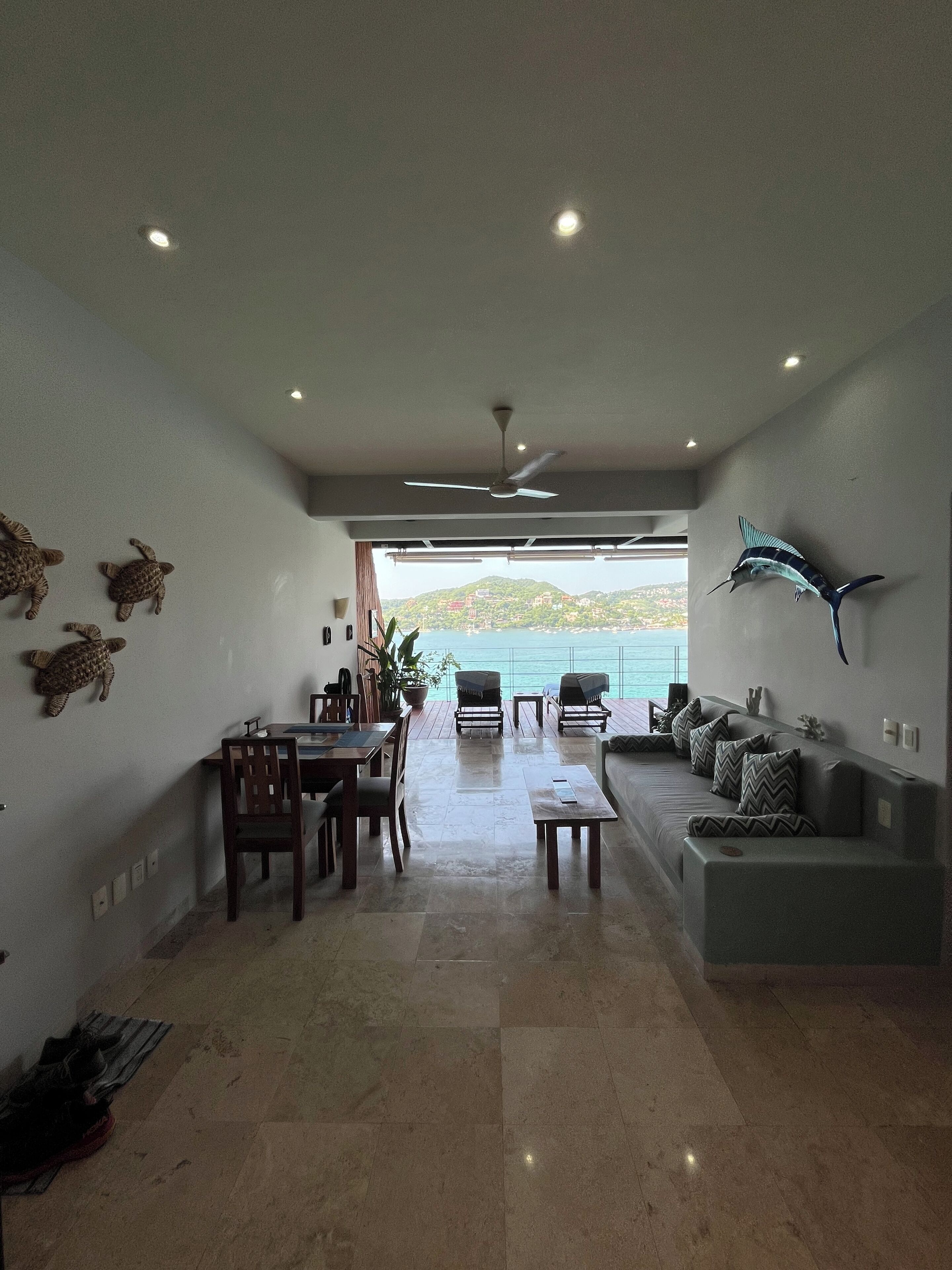 A spacious living area with a dining table, chairs, a sofa, and a view of the sea.