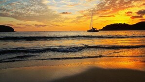 Un coucher de soleil sur une plage, avec un voilier à l'horizon.