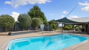 Una piscina con un patio techado, rodeada de árboles y una valla.