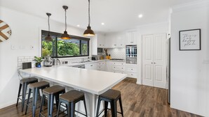 Una cocina moderna con una isla grande, taburetes de bar, iluminación colgante y armarios blancos.