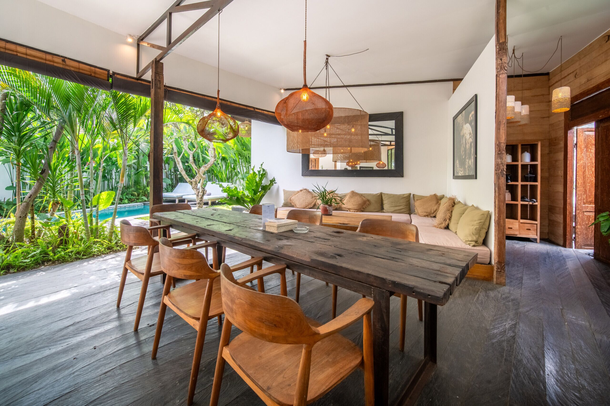 Une pièce spacieuse avec une grande table à manger en bois, des chaises en bois, un canapé avec des coussins et un luminaire suspendu.