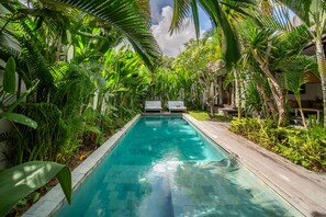 A rectangular swimming pool surrounded by lush tropical plants and wooden deck. - Designer 3BR Villa - Exquisite Canggu Retreat (Kecamatan Kuta Utara)