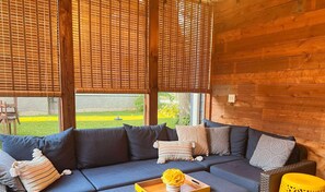 An enclosed patio with a blue sofa, cushions, and a tray with flowers. - Cozy Crystal Lakefront Cottage (Plymouth)