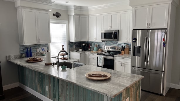 A modern kitchen with white cabinets, a central island, stainless steel appliances, and a backsplash with blue tiles. - Promise Land Gem (Morehead City)