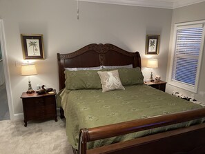 A bedroom with a wooden bed, green bedding, two bedside tables with lamps, and framed pictures on the walls.
