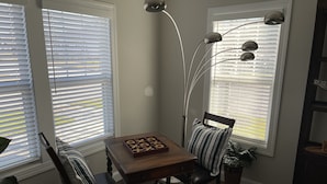 A dining area with a wooden table, two chairs, a board game, and a tall floor lamp. - Promise Land Gem (Morehead City)