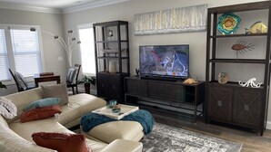 A living room with a beige sofa, a coffee table, a TV, and a bookshelf. - Promise Land Gem (Morehead City)
