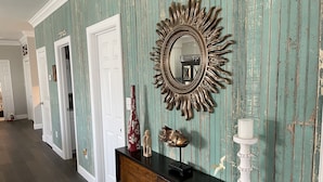 A hallway with teal wallpaper, a sunburst mirror, a black console table with decorative items, and white doors. - Promise Land Gem (Morehead City)