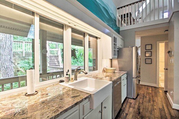 Enjoy a kitchen with a large window offering a view of the outdoors, featuring a granite countertop, stainless steel sink, and white cabinetry.