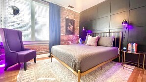 A bedroom with a bed, a chair, a small table, a lamp, and a wall-mounted TV. - The Dim Light Lower Town Luxury Boutique Condos (Paducah)