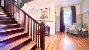 A staircase with wooden steps and a black handrail, a framed picture on the wall, a window with curtains, and a blue armchair. - The Dim Light Lower Town Luxury Boutique Condos (Paducah)