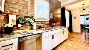 A kitchen with a brick wall, wooden cabinets, a large window, and a dishwasher. - The Dim Light Lower Town Luxury Boutique Condos (Paducah)