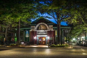 Un edificio con un cartel luminoso, una entrada protegida por una reja y una calle con coches aparcados.