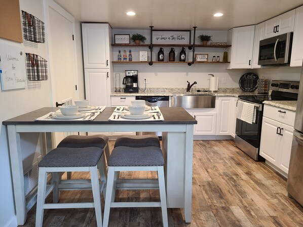 A modern kitchen with white cabinets, a central island with stools, a coffee station, and a stainless steel sink. - Haney Hideaway (Colorado Springs)