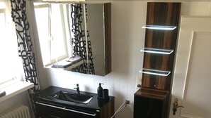 A modern bathroom with a black tiled floor, a sink with a mirror above, and a wooden cabinet with built-in lighting. - ARTHUR Historic vacation home Moselle (Mülheim (Mosel))