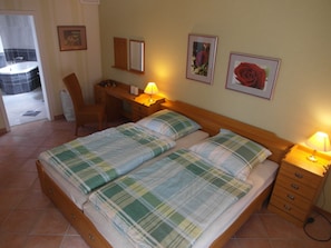 A bedroom with two beds, a desk, a chair, and a bathroom visible in the background.