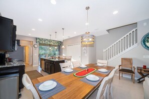 A modern kitchen with a dining area, featuring a wooden table set for four, white chairs, and a staircase leading to another level.