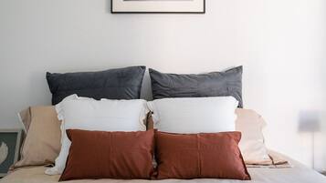 Una cama bien hecha con una variedad de almohadas y una manta, un cuadro abstracto enmarcado en la pared y una revista sobre la cama.