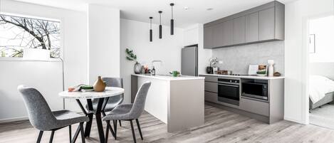 A modern kitchen with grey cabinets, a central island, and a dining area with grey chairs.
