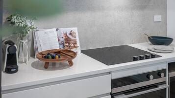 Una cocina con encimera blanca, placa de inducción negra, estante de madera para especias, un florero con flores y un libro de cocina.