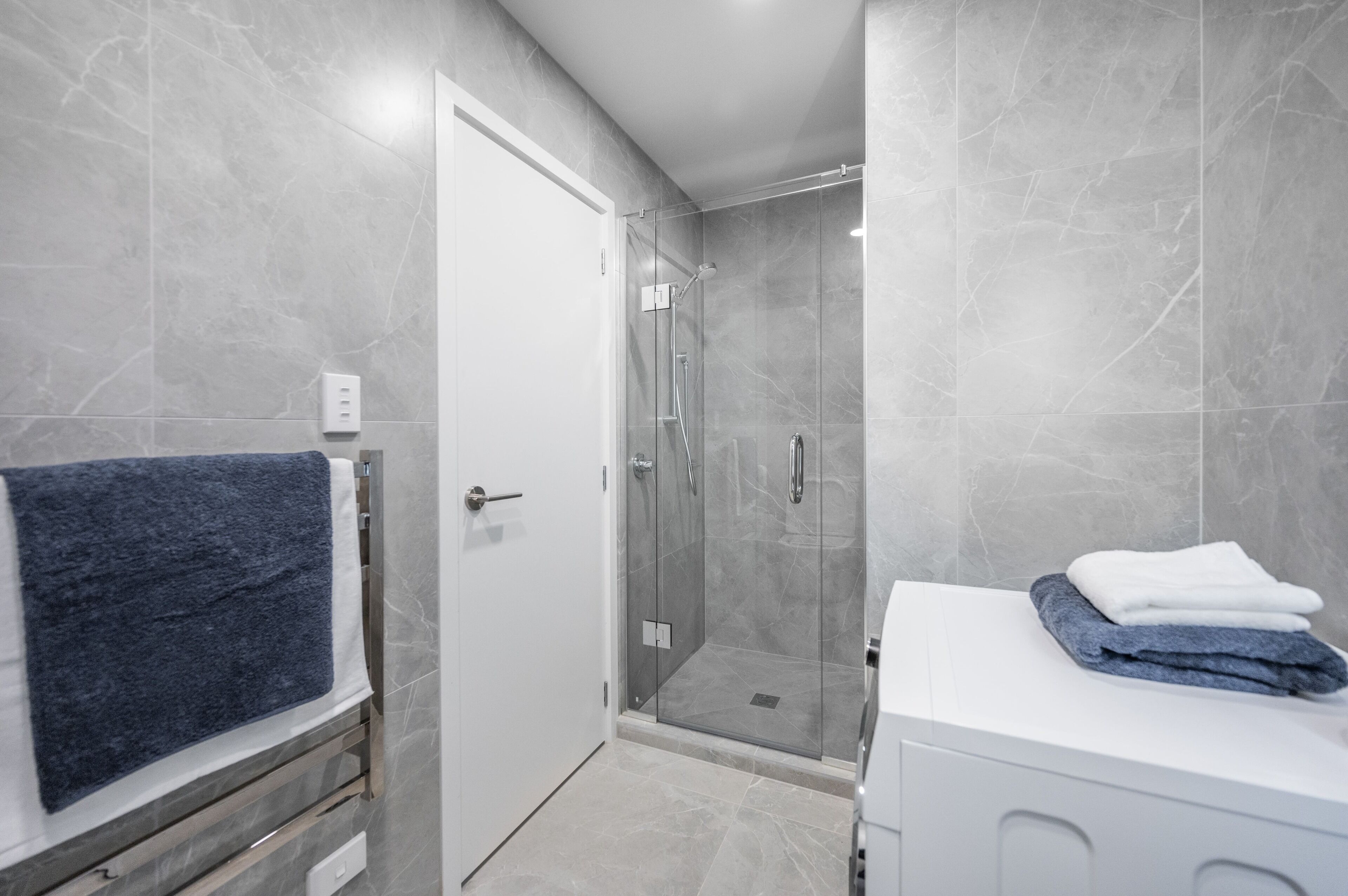 Une salle de bain moderne avec une douche à parois de verre, un lavabo blanc et un porte-serviettes avec une serviette bleue.