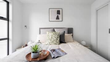 A modern bedroom with a bed, a bedside table with a plant, a magazine, and a framed picture on the wall.