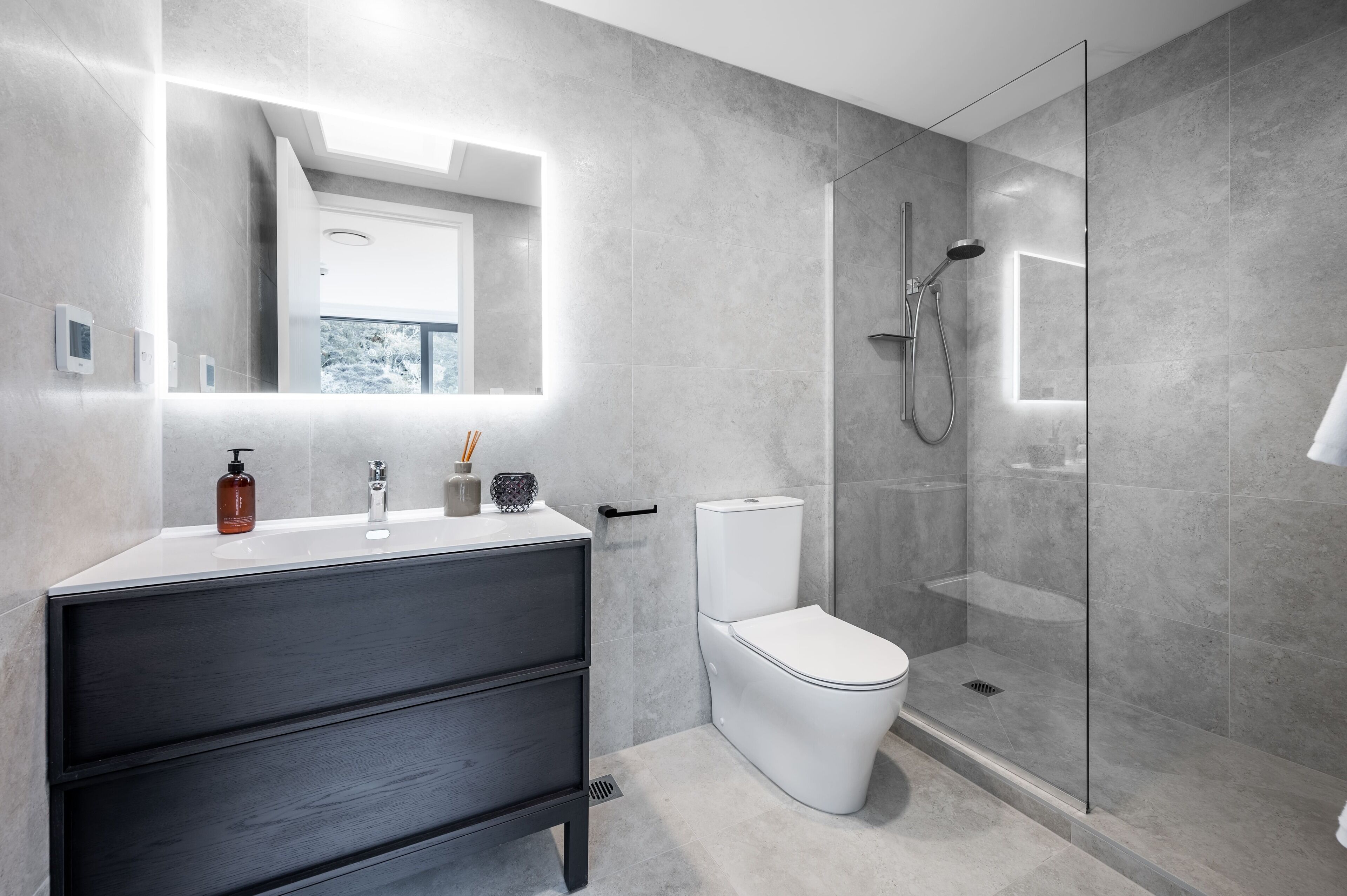 Een moderne badkamer met een donker houten wastafelmeubel, een wit toilet en een douchecabine met glazen wanden.
