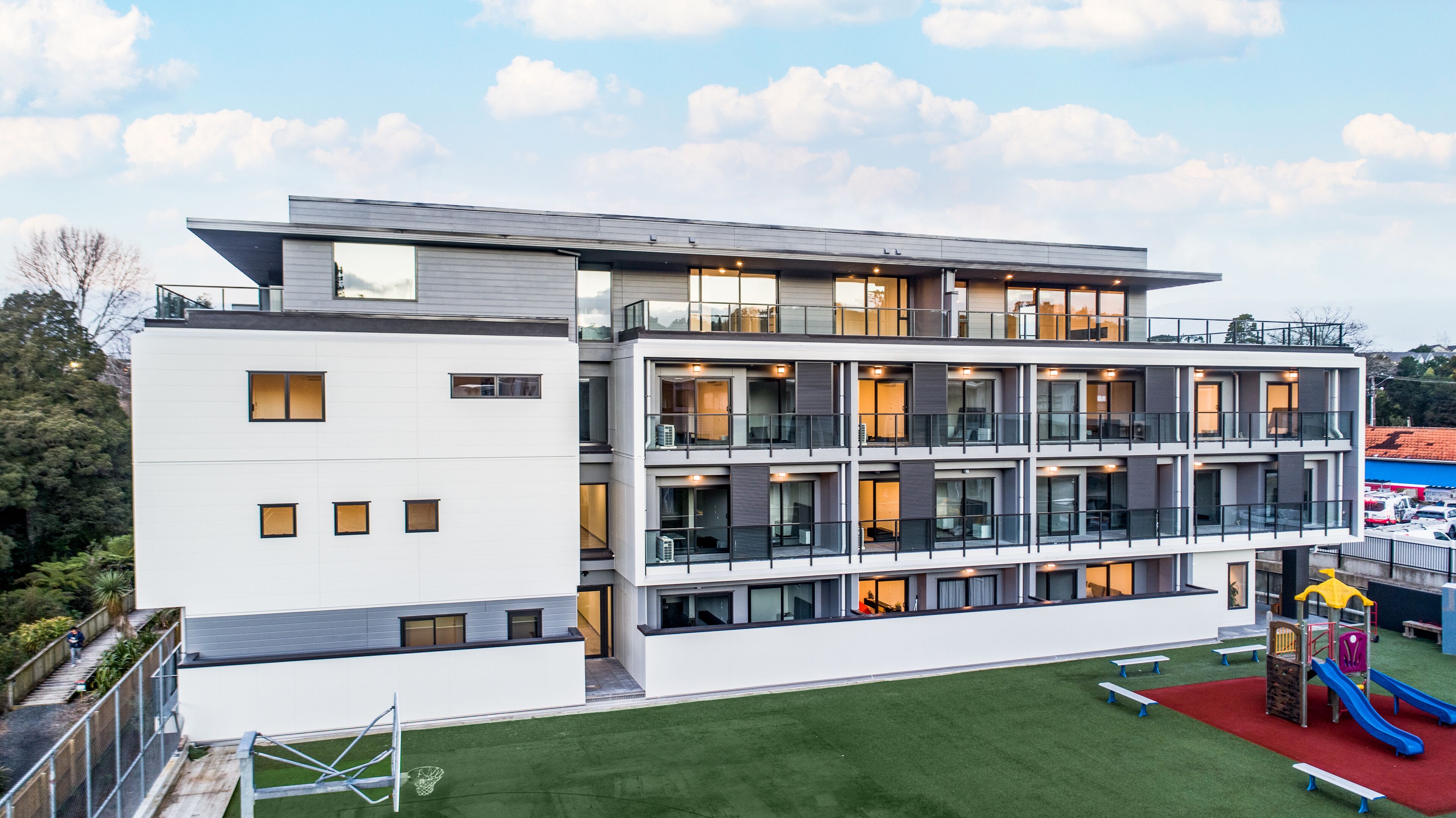 Un edificio de varios pisos con balcones, ventanas amplias y una zona de juegos con toboganes y bancos.