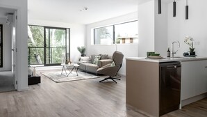 Une cuisine moderne équipée d’un lave-vaisselle, un coin repas avec un canapé et une table basse, et de grandes fenêtres offrant une vue sur l’extérieur.