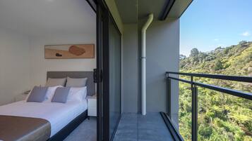 A modern bedroom with a bed, a bedside table, a painting on the wall, and a balcony with a view of a lush landscape.