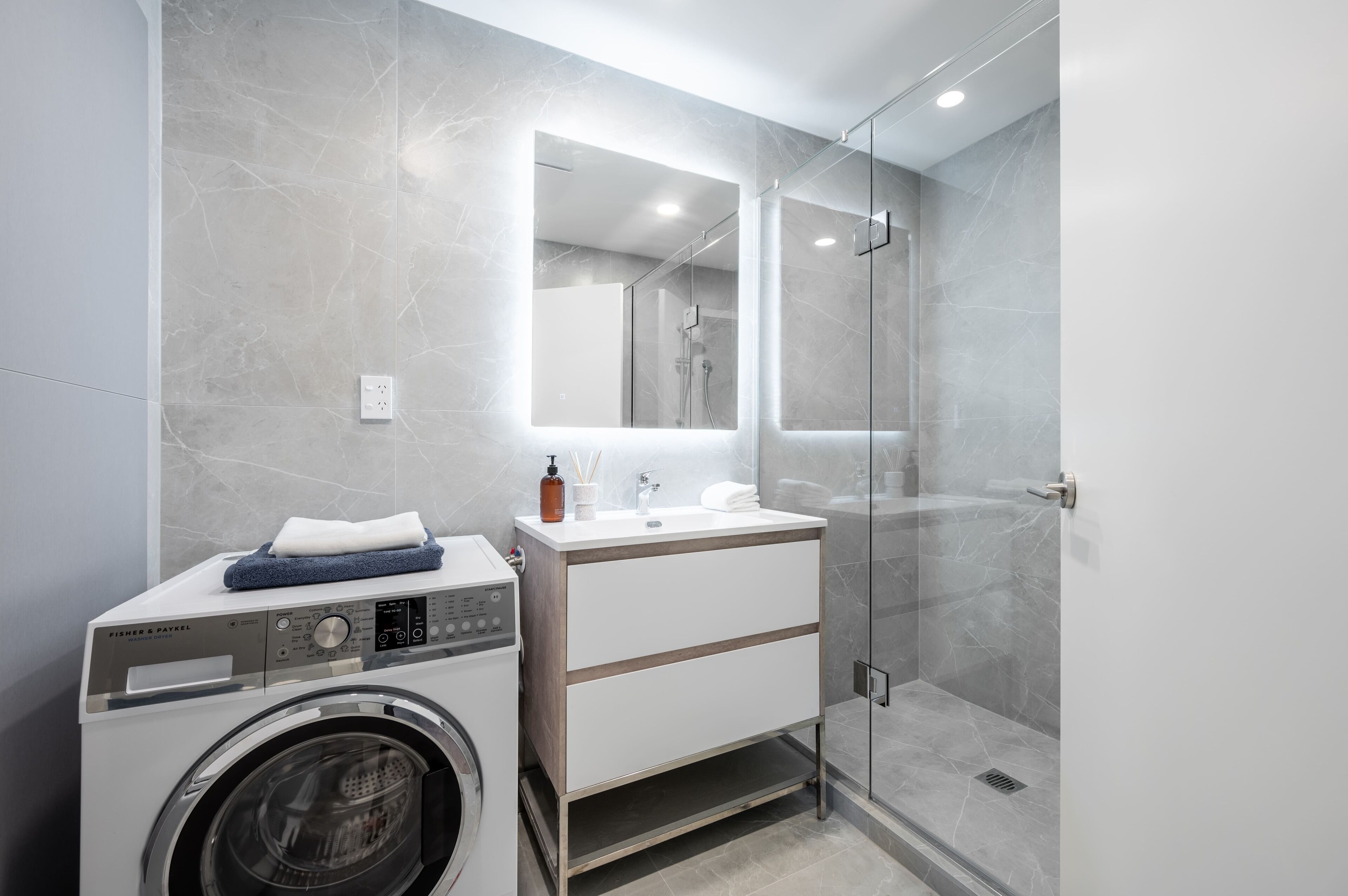 A modern bathroom with a washing machine, a vanity with a mirror, and a glass shower enclosure.
