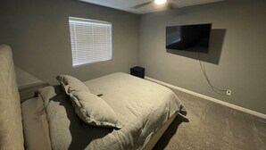 A bedroom with a bed, a ceiling fan, a window with blinds, and a mounted TV. - Sweet Little Paradise - Short Term / Long Term Renting   (Phoenix)