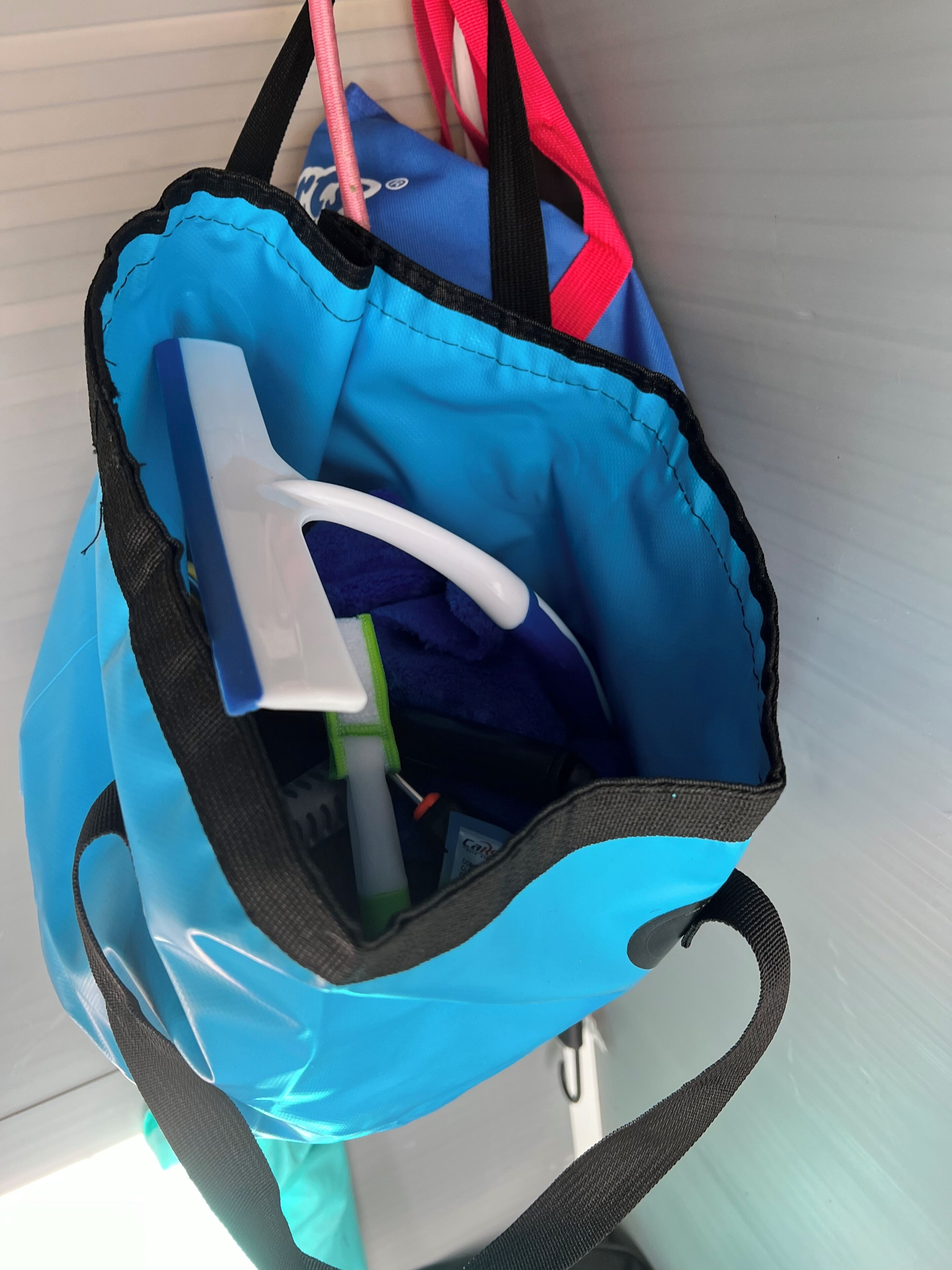 A blue bag with a white handle and a black strap, containing a green bottle and a white object.