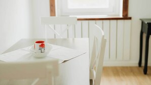 A white dining table with a white chair, a small white bowl with a red object, and a window with a wooden frame. - Lovingly furnished guest apartments Alpirsbach - Apartment 1 (Alpirsbach)