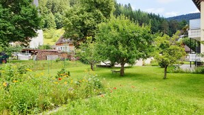 A lush garden with a variety of flowers and trees, a bench, and a small building with a sloped roof. - Lovingly furnished guest apartments Alpirsbach - Apartment 1 (Alpirsbach)