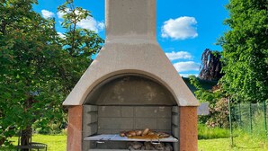 A stone-built outdoor pizza oven with a chimney, surrounded by a grassy area and trees. - Lovingly furnished guest apartments Alpirsbach - Apartment 1 (Alpirsbach)