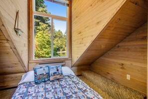 A bedroom with a large window, wooden walls, and a bed with a patterned quilt.