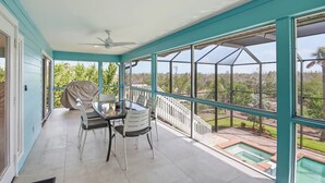 Eine überdachte Terrasse mit Tisch und Stühlen, einem Deckenventilator und Blick auf einen Pool und Grünflächen.