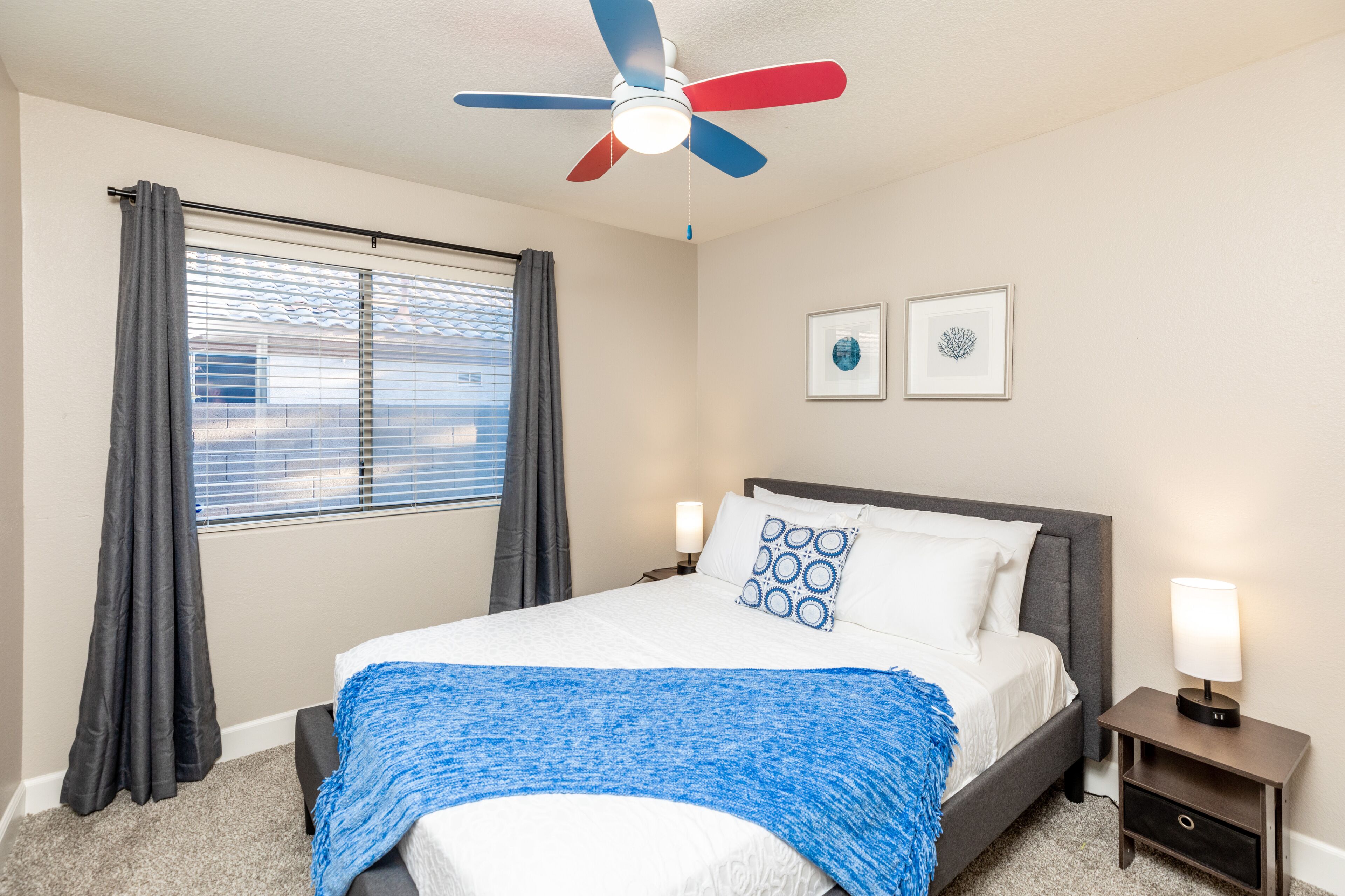 A bedroom with a bed, a ceiling fan, a nightstand, and a window with curtains.