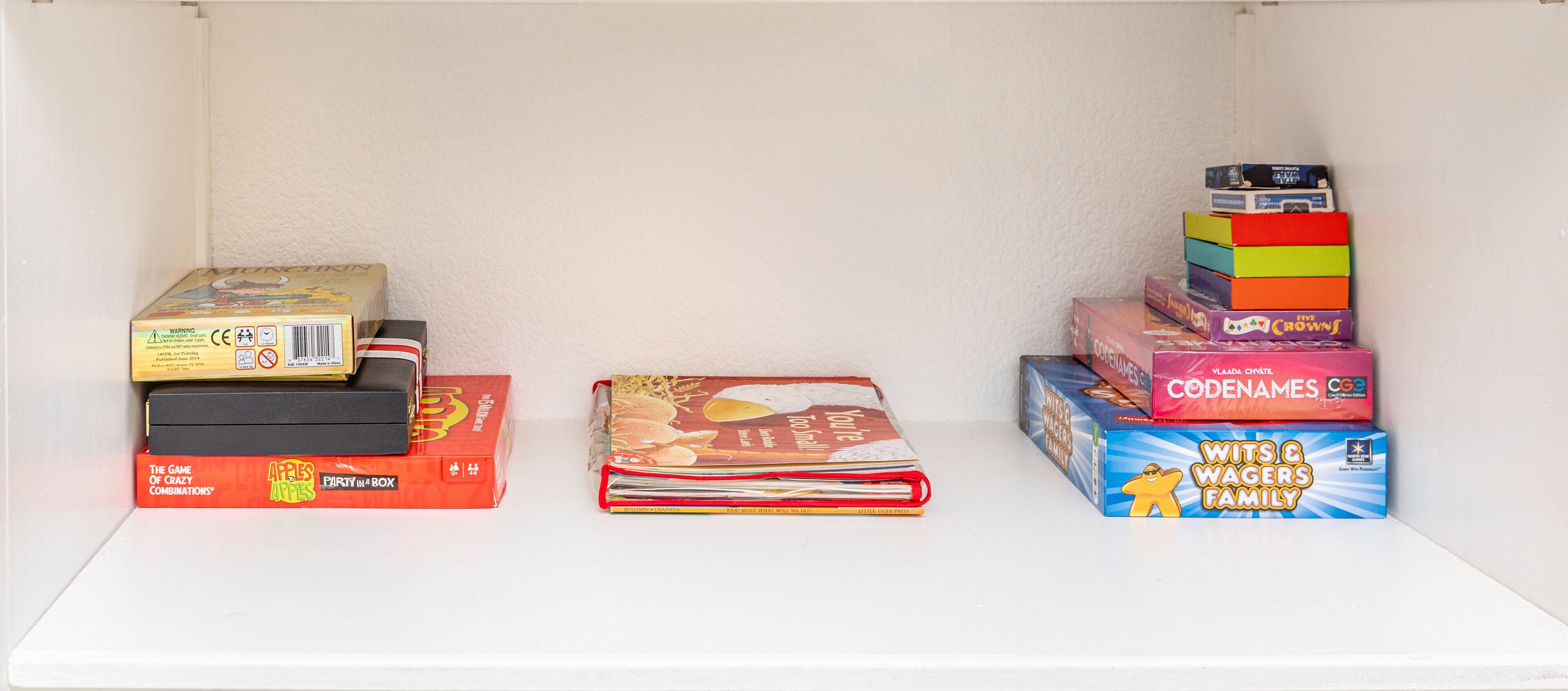A shelf with various board games, including 'Apples to Apples', 'Party in a Box', 'Five Crows', and 'Wits & Wagers Family'.