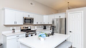 A modern kitchen with white cabinetry, stainless steel appliances, and a central island with a vase of flowers. - Golf and Backyard Getaway (Mesa)