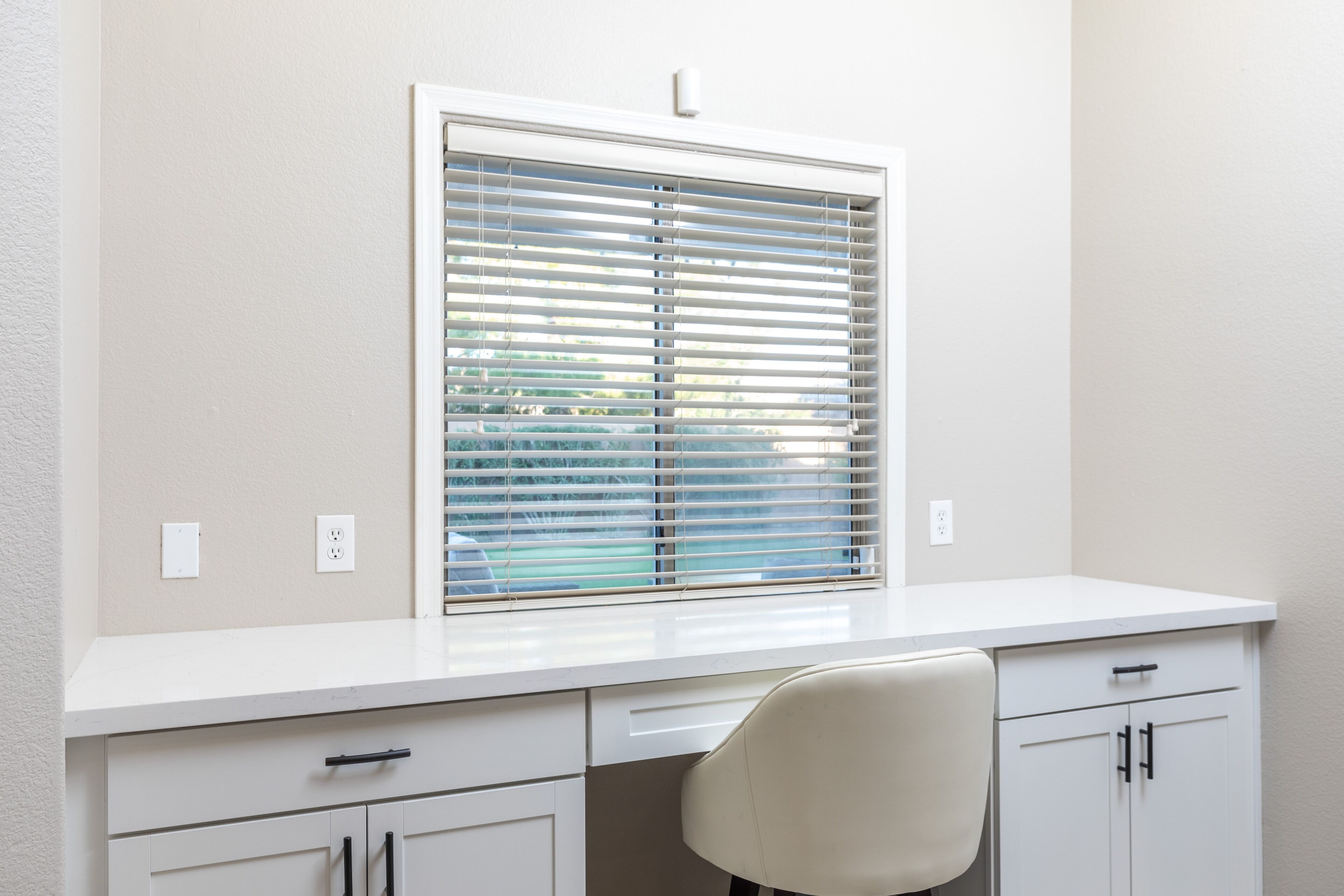 A white desk with a window, a chair, and a cabinet.
