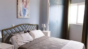 Una camera da letto con un letto, comodini, una lampada da comodino, un lampadario, un armadio e una finestra con tende.