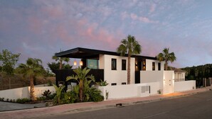 A modern two-story house with a flat roof, large windows, and a well-maintained garden with palm trees and other plants. - Estepona - Sleeps 8 - Pool - Pet Friendly - Garden (Estepona)