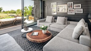 A modern living room with a grey sectional sofa, a round wooden coffee table, and a large window overlooking a garden. - Estepona - Sleeps 8 - Pool - Pet Friendly - Garden (Estepona)